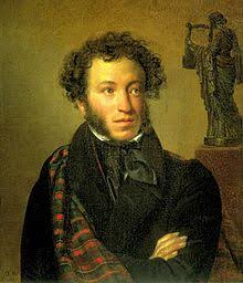Retrato de un hombre joven con cabello rizado y barba ligera, usando un abrigo oscuro y una bufanda. Al fondo, hay una estatua de una figura femenina.