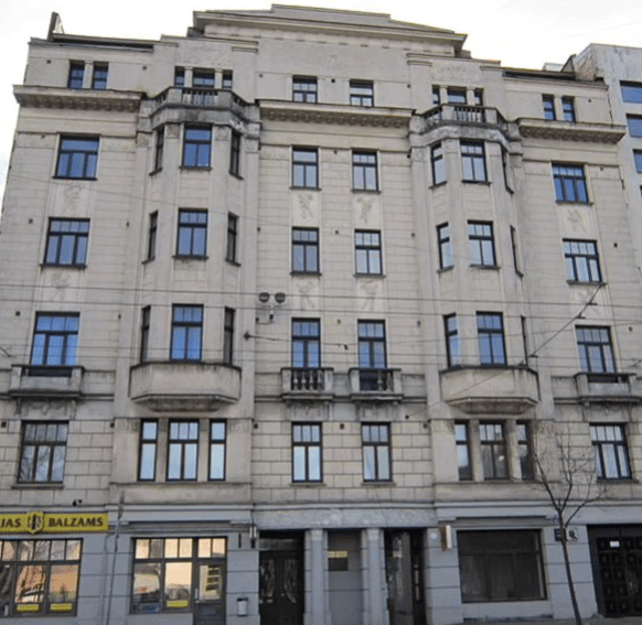 Fachada de un edificio de estilo clásico con varios pisos y ventanas simétricas, algunos detalles arquitectónicos en la parte superior.