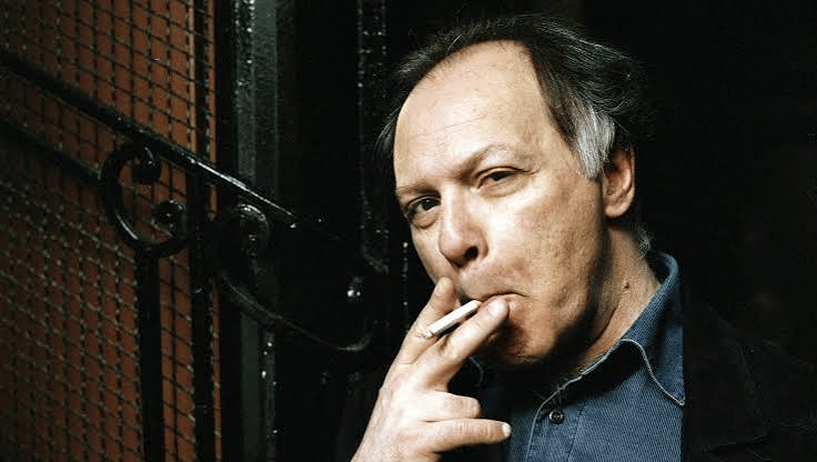 Retrato de un hombre con cabello oscuro, sosteniendo un cigarrillo en la mano y mirando hacia la cámara.