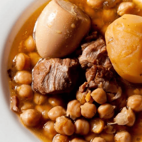 Plato de garbanzos con carne, huevos y patatas en un caldo sustancioso.