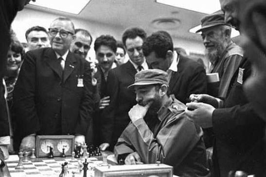Fidel Castro concentrado en una partida de ajedrez rodeado de varios espectadores, en una imagen en blanco y negro que muestra un ambiente de tensión y atención.