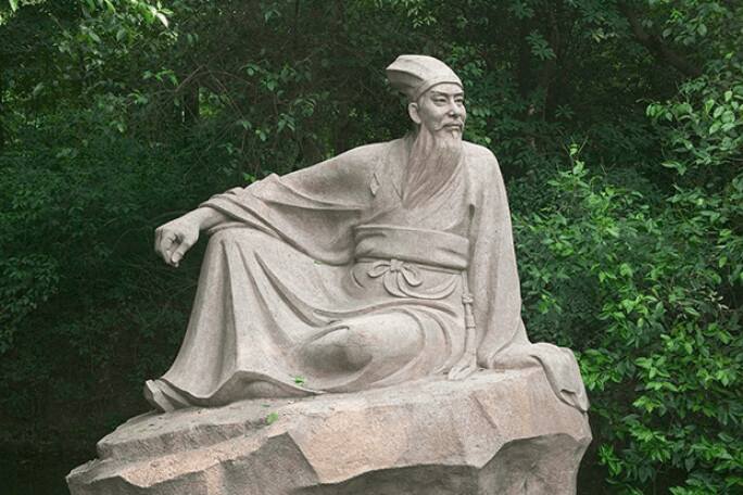 Escultura de un sabio sentado sobre una roca, con vestimenta tradicional, rodeado de vegetación.
