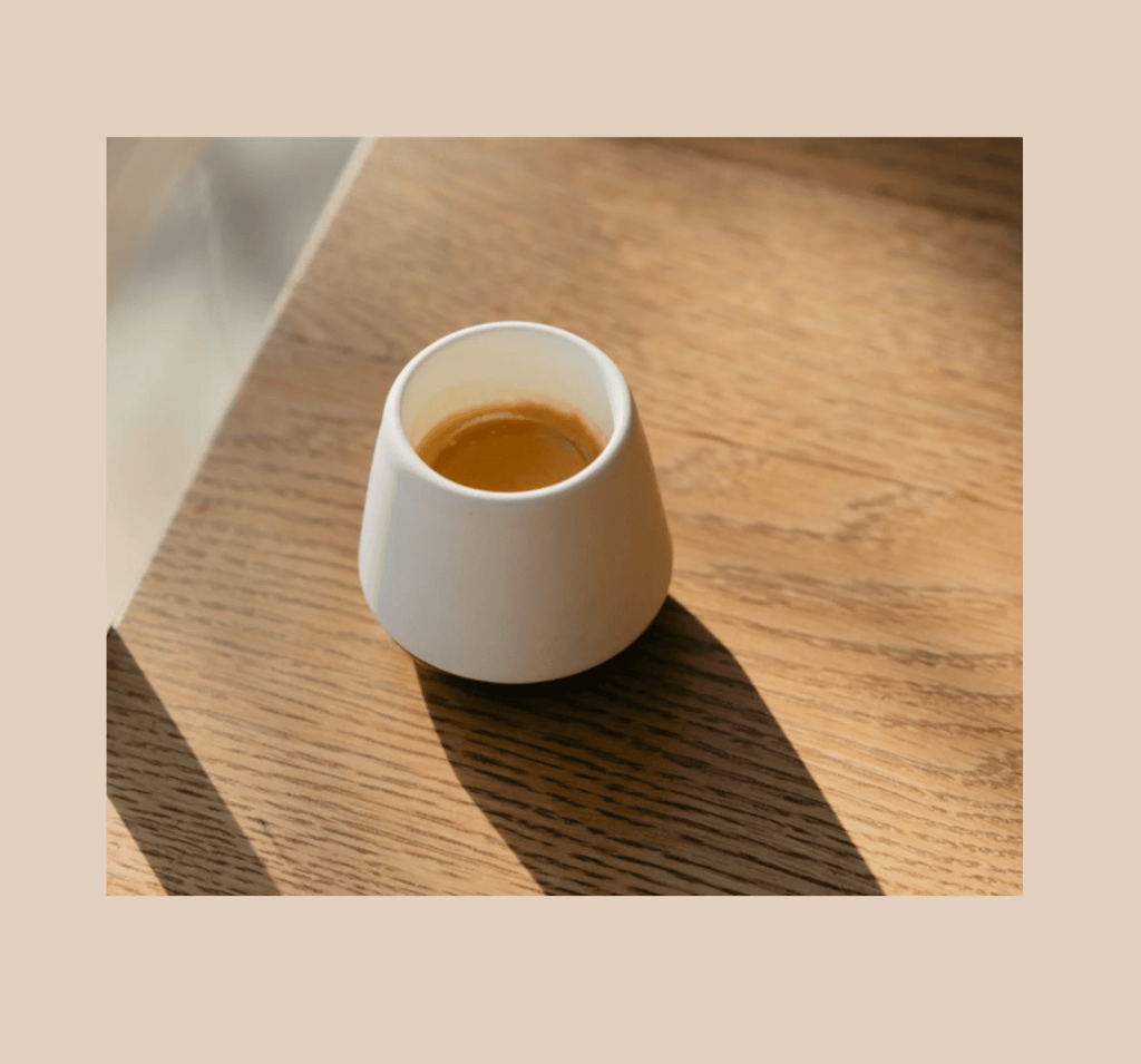 Taza blanca con café sobre una mesa de madera iluminada por la luz del sol.