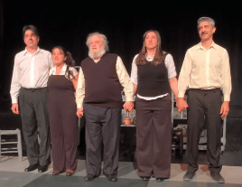 Cinco actores en el escenario sosteniendo las manos juntos, con vestimenta formal y expresiones de satisfacción.