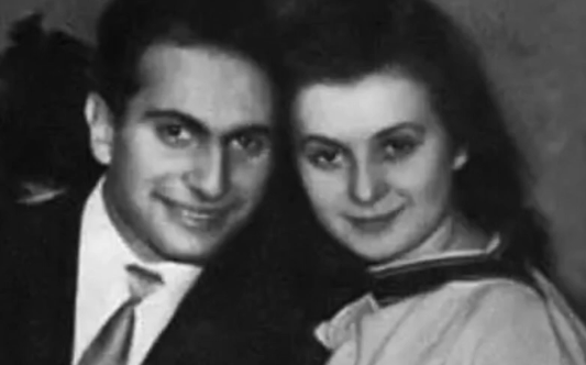 Una pareja sonriente posando juntos en una fotografía en blanco y negro, con el hombre vestido con un traje y corbata y la mujer con una blusa clara.