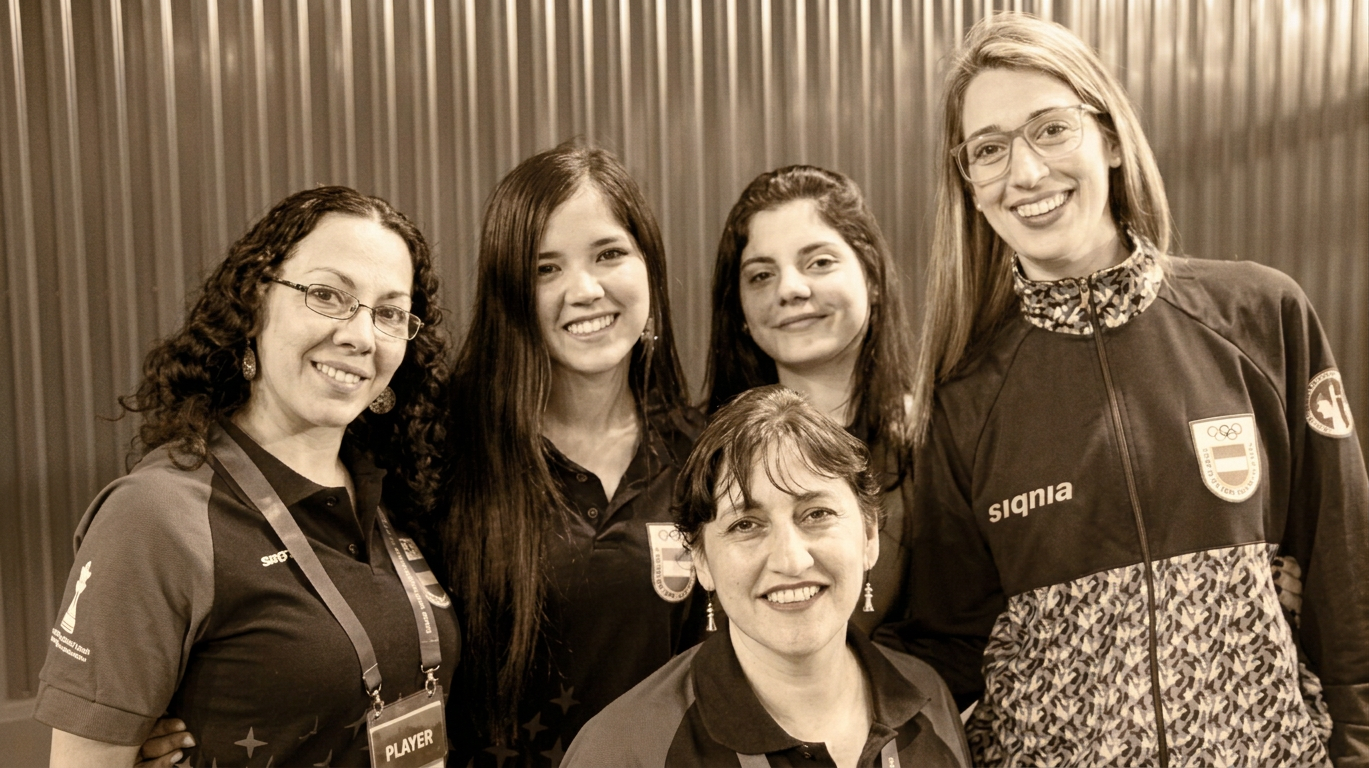 Grupo de cinco mujeres sonriendo, vestidas con camisetas y chaquetas deportivas, en un ambiente amistoso.