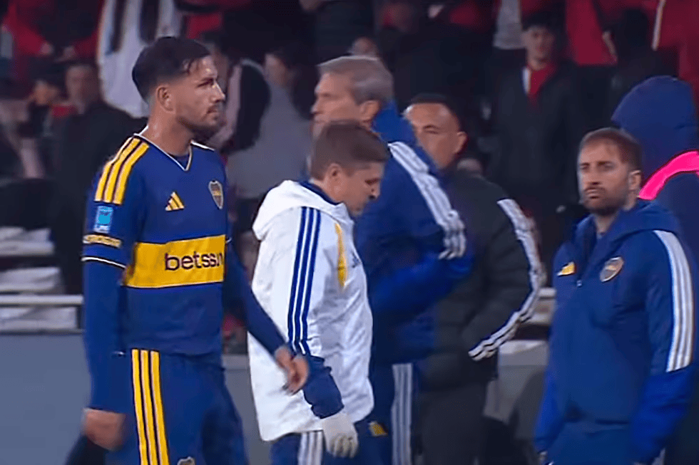 Jugadores del equipo Boca Juniors en la zona de cambios durante un partido de fútbol, con un ambiente de tensión en el estadio.
