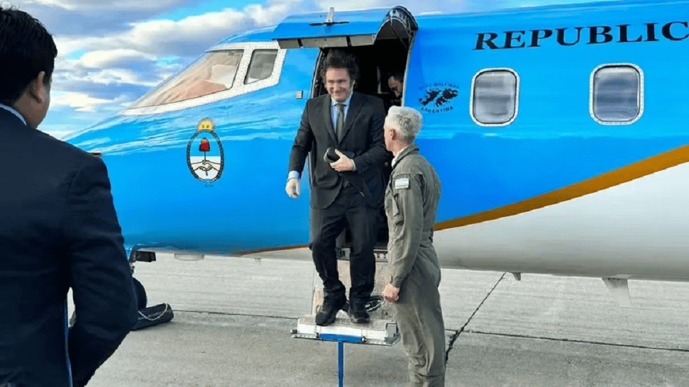 Un hombre en traje baja de un avión pequeño de color azul con el texto 'REPÚBLICA' en el costado, mientras dos personas lo observan en un aeropuerto.