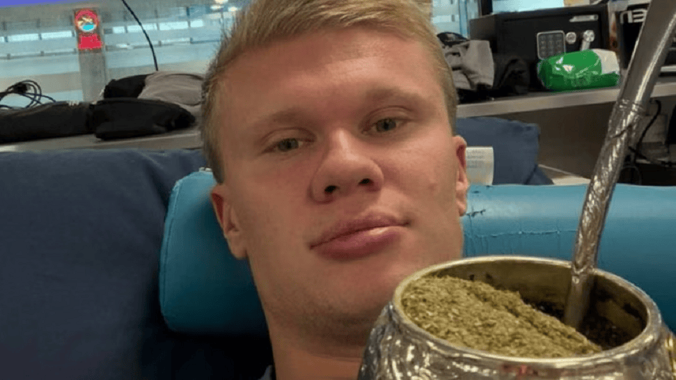 Joven sosteniendo un mate con yerba en un ambiente interior, mirando a la cámara.