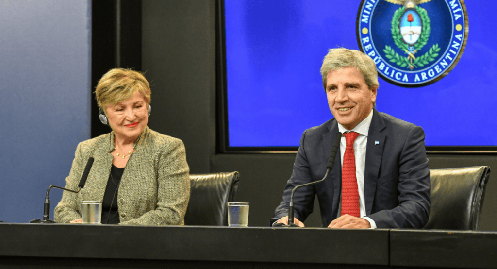 Dos funcionarios en una conferencia de prensa, uno mirando hacia el público y el otro sonriendo. Fondo con el escudo de la República Argentina.