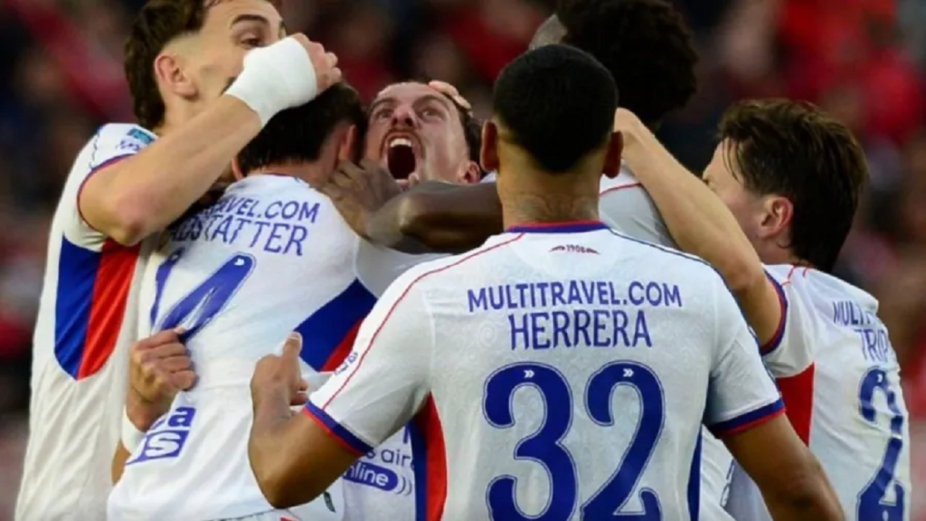Jugadores de fútbol celebrando un gol, abrazándose y mostrando alegría en el campo.