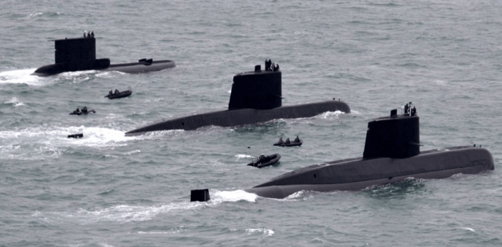 Tres submarinos en el mar, con personas en la superficie y botes cercanos.