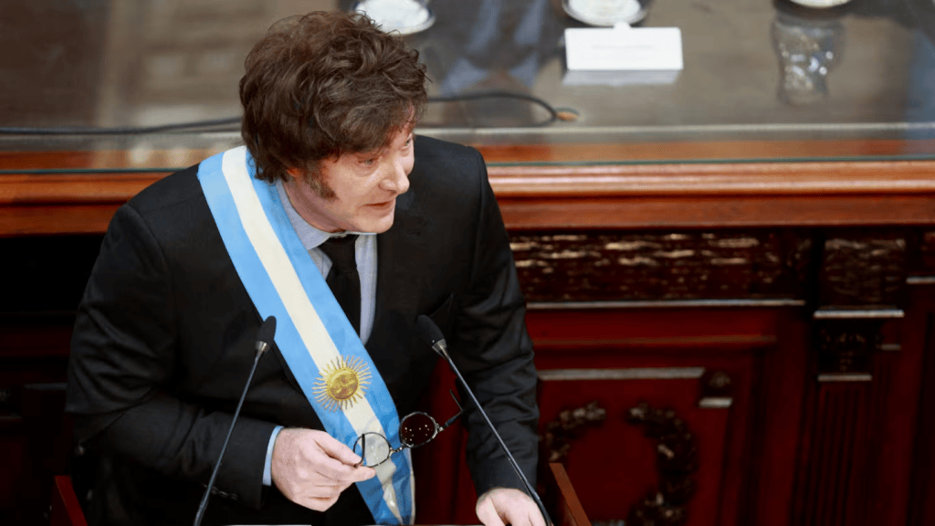 Un hombre con cabello rizado y una banda presidencial argentina, hablando en un podio del Congreso.