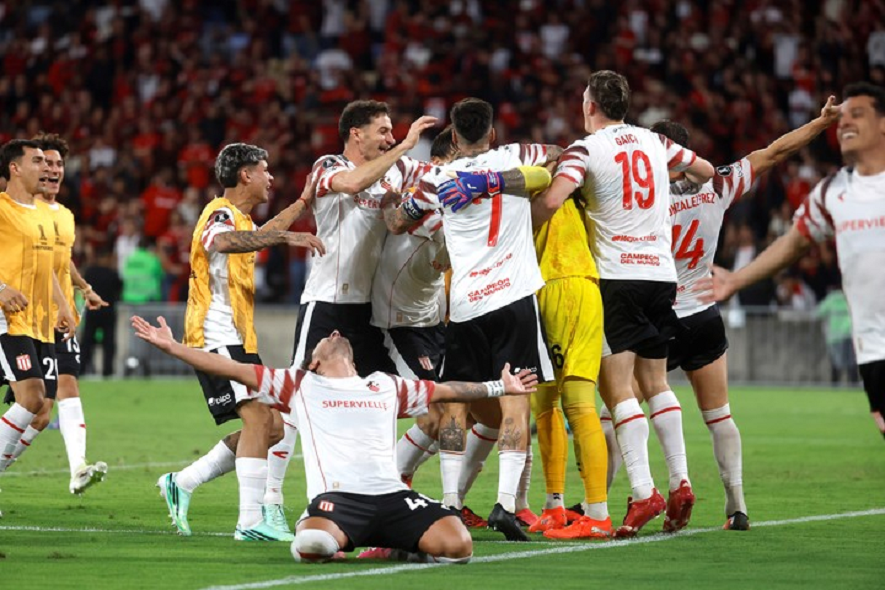 Jugadores de un equipo de fútbol celebrando un gol en un partido, con un ambiente de euforia en el estadio.