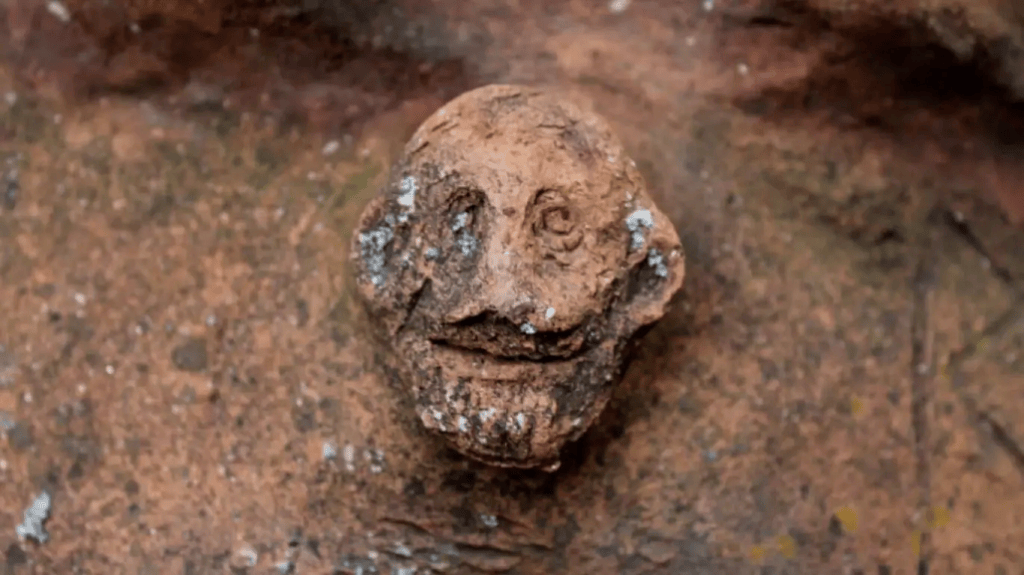 Escultura en relieve de una cara sonriente en una superficie de arcilla.