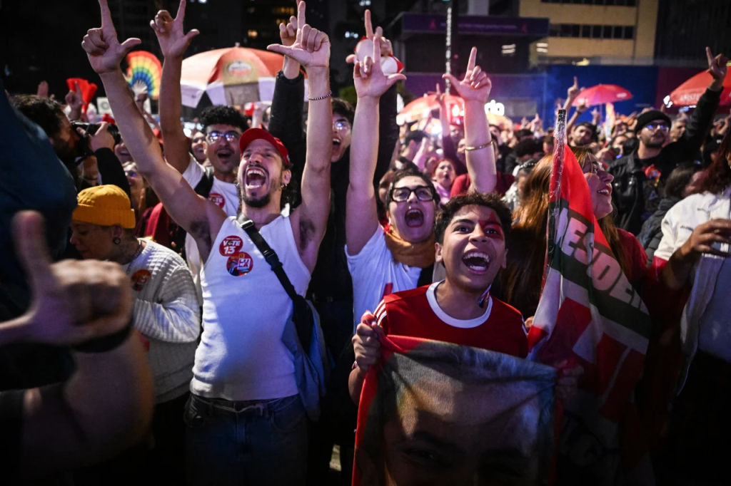 Multitud de personas animadas y emocionadas en un evento, levantando las manos y banderas, mostrando entusiasmo y apoyo.