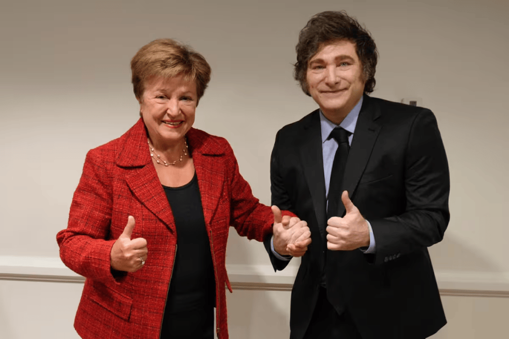 Una mujer y un hombre posando juntos, ambos sonriendo y mostrando el pulgar hacia arriba. La mujer lleva una chaqueta roja y el hombre un traje negro.
