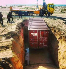 Un contenedor rojo siendo levantado por una grúa sobre un hoyo en la tierra en un paisaje desértico.