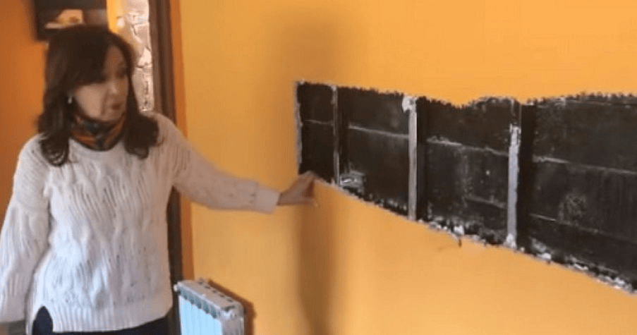 Mujer señalando una pared con marcas negras y una pintura naranja de fondo, evidenciando trabajos de reparación.